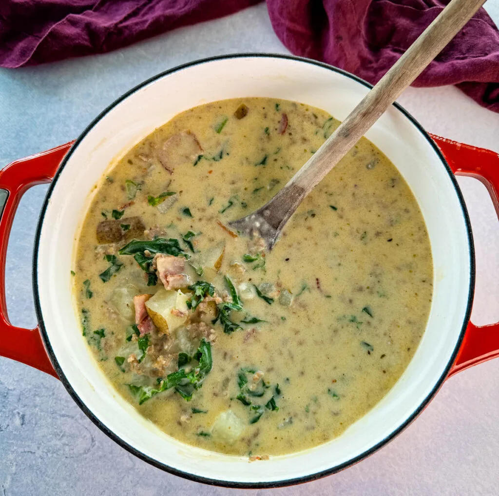 Italian sausage soup with potatoes and kale in a Dutch oven with a wooden spoon