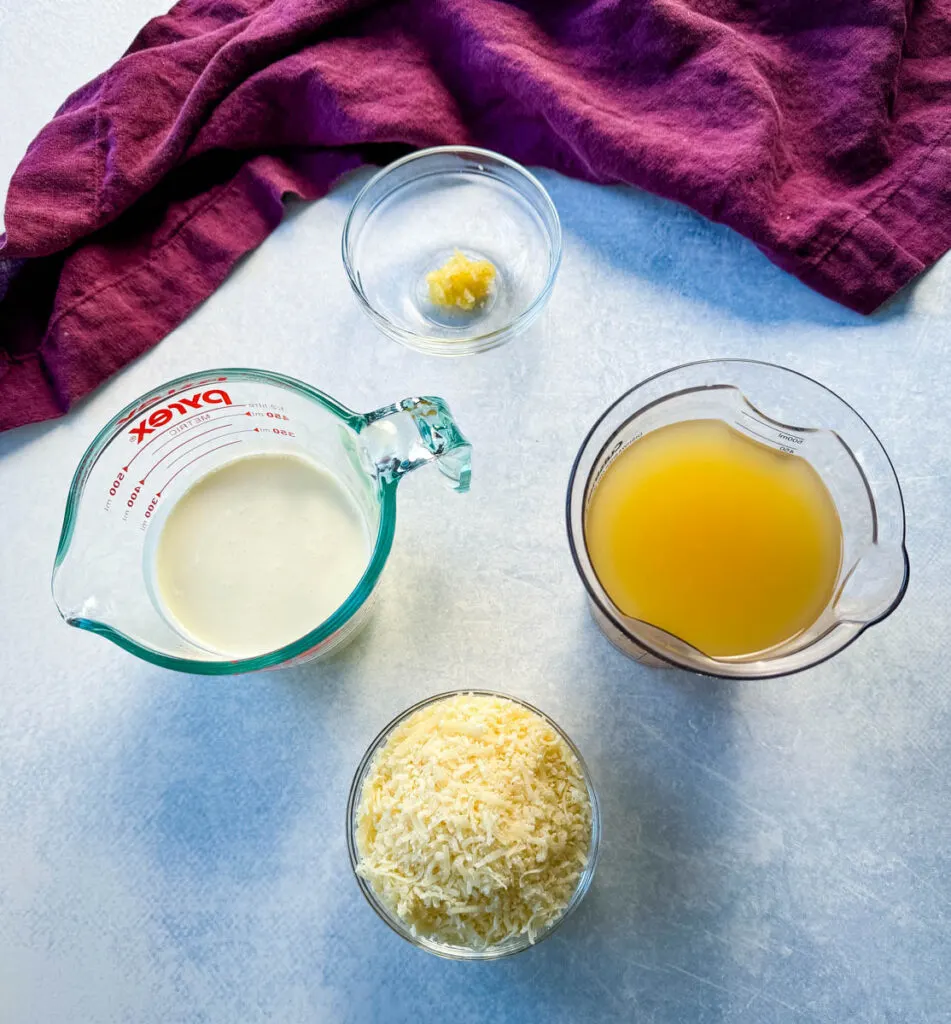 minced garlic, heavy cream, broth, and grated Parmesan cheese in separate glass bowls