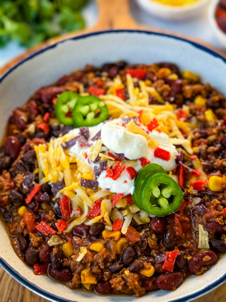 beef taco chili in a white bowl with jalapenos, sour cream, shredded cheese, and tortilla chips