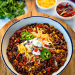 beef taco chili in a white bowl with jalapenos, sour cream, shredded cheese, and tortilla chips