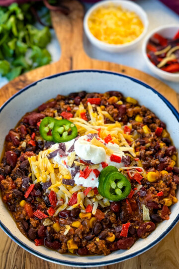 beef taco chili in a white bowl with jalapenos, sour cream, shredded cheese, and tortilla chips