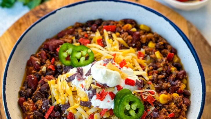 beef taco chili in a white bowl with jalapenos, sour cream, shredded cheese, and tortilla chips