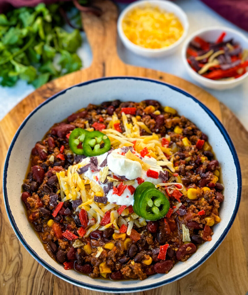 beef taco chili in a white bowl with jalapenos, sour cream, shredded cheese, and tortilla chips