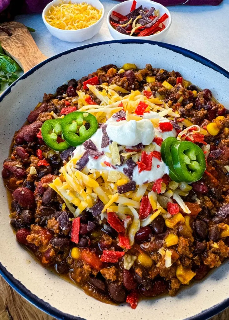 beef taco chili in a white bowl with jalapenos, sour cream, shredded cheese, and tortilla chips