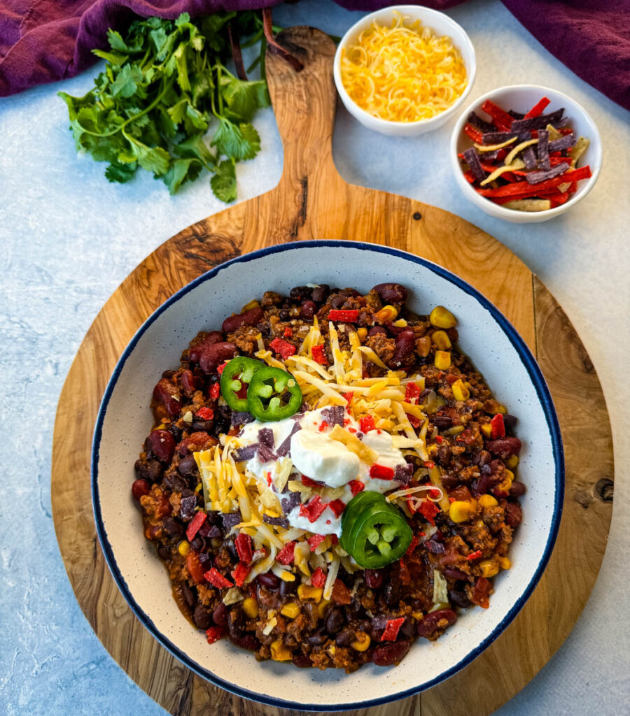 beef taco chili in a white bowl with jalapenos, sour cream, shredded cheese, and tortilla chips