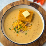 beer cheese soup with bacon, shredded cheese, green onions, and a slice of sweet potato cornbread in a white bowl