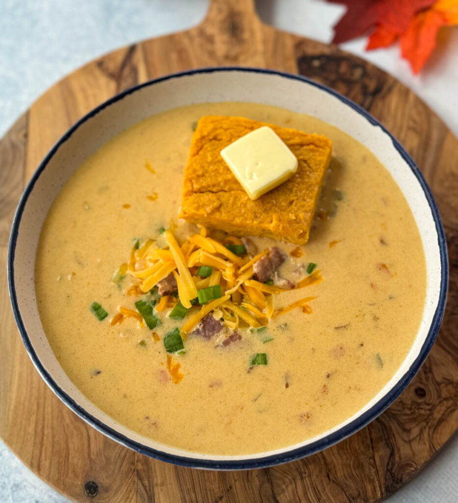 beer cheese soup with bacon, shredded cheese, green onions, and a slice of sweet potato cornbread in a white bowl