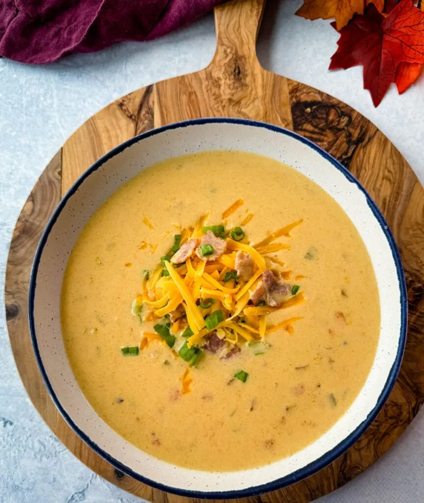 beer cheese soup with bacon, shredded cheese, and green onions in a white bowl