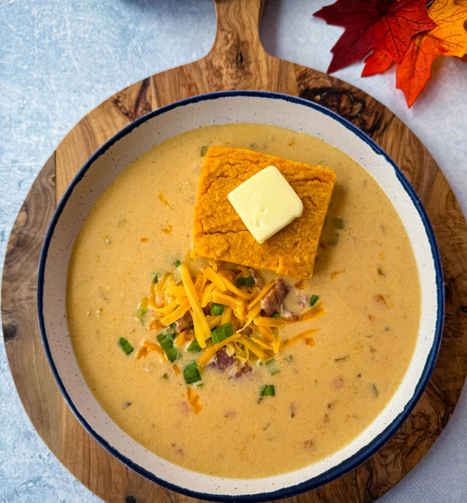 beer cheese soup with bacon, shredded cheese, green onions, and a slice of sweet potato cornbread in a white bowl