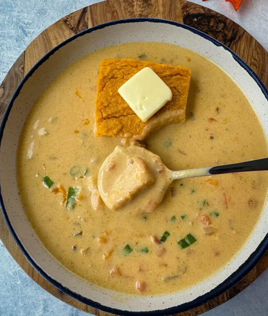 beer cheese soup with bacon, shredded cheese, green onions, and a slice of sweet potato cornbread in a white bowl