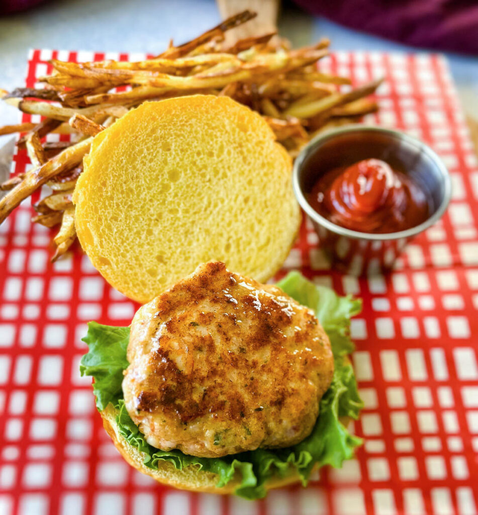 shrimp burger with lettuce, tomato, and spicy mayo on a plate with fries and ketchup