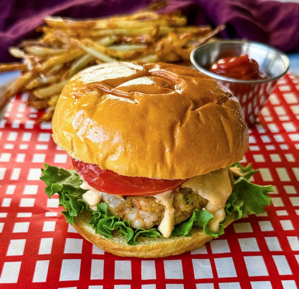 shrimp burger with lettuce, tomato, and spicy mayo on a plate with fries and ketchup