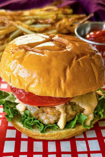 shrimp burger with lettuce, tomato, and spicy mayo on a plate with fries and ketchup