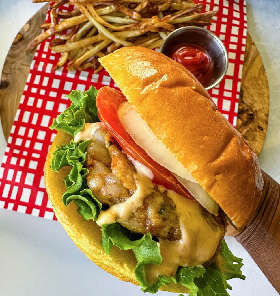 person holding shrimp burger with lettuce, tomato, and spicy mayo