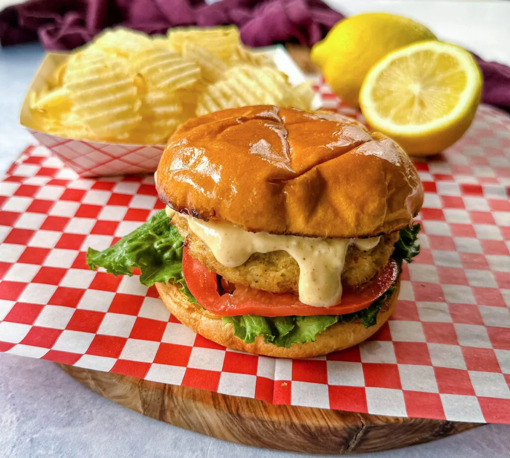 crab cake sandwich on a brioche bun with lettuce tomatoes and a side of chips with remoulade sauce