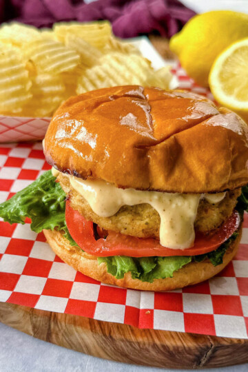 crab cake sandwich on a brioche bun with lettuce tomatoes and a side of chips with remoulade sauce