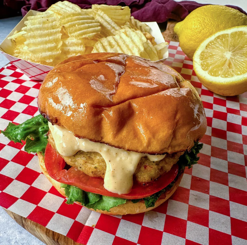 crab cake sandwich on a brioche bun with lettuce tomatoes and a side of chips with remoulade sauce