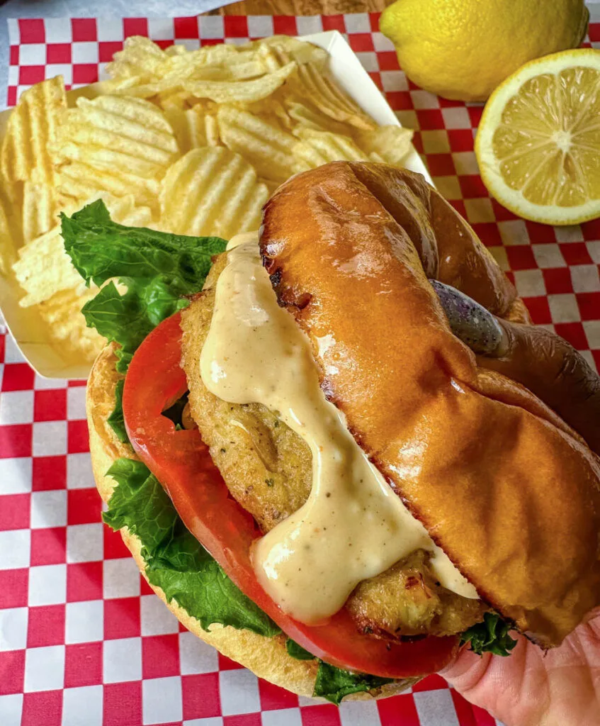 person holding crab cake sandwich with chips