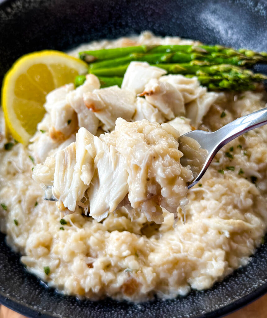 a fork full of crab risotto in a black bowl