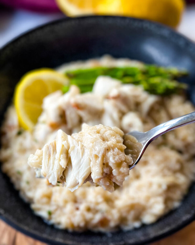 a fork full of crab risotto in a black bowl