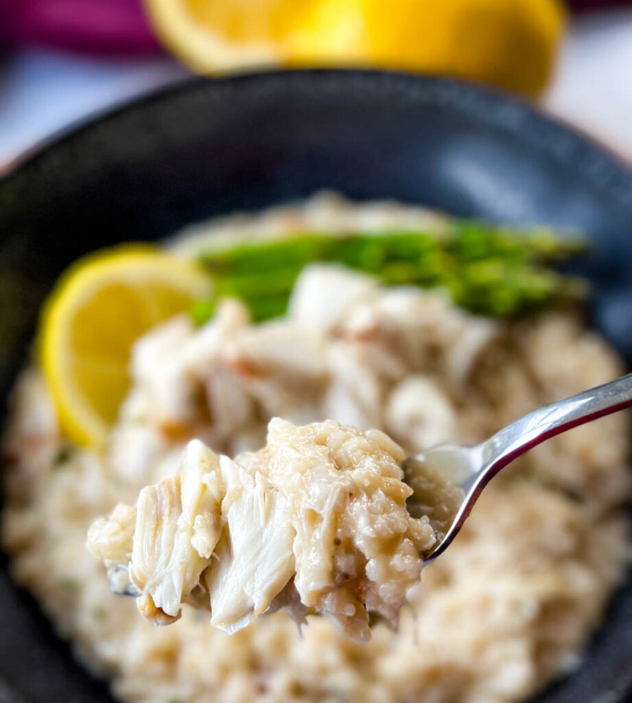 a fork full of crab risotto in a black bowl