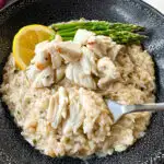 crab risotto in a black bowl with fresh lemon and asparagus