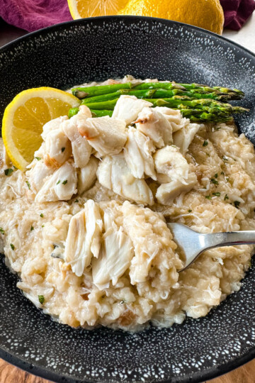 crab risotto in a black bowl with fresh lemon and asparagus