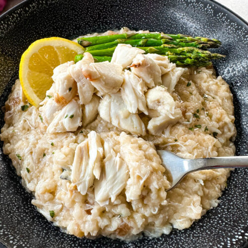 crab risotto in a black bowl with fresh lemon and asparagus