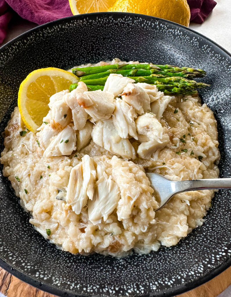 crab risotto in a black bowl with fresh lemon and asparagus