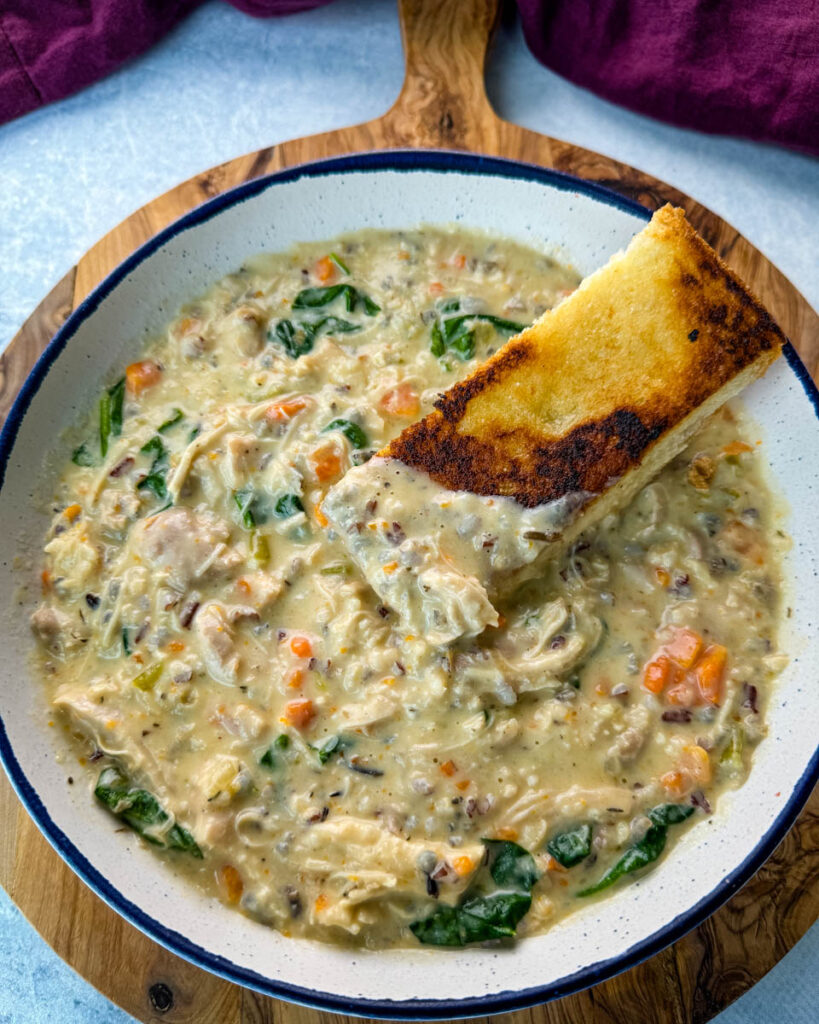 chicken wild rice soup in a white bowl with a slice of toasted bread