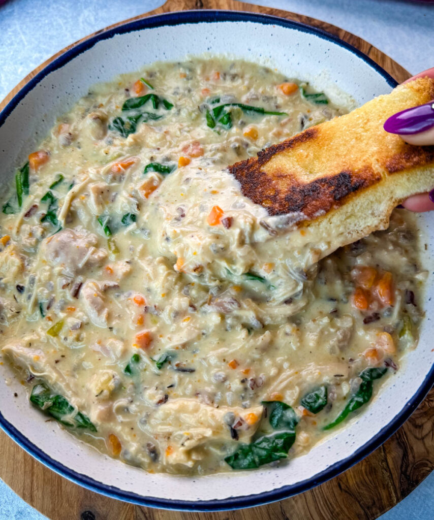 chicken wild rice soup in a white bowl with a slice of toasted bread