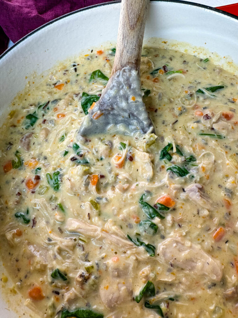 creamy chicken wild rice soup in a red Dutch oven with a wooden spoon