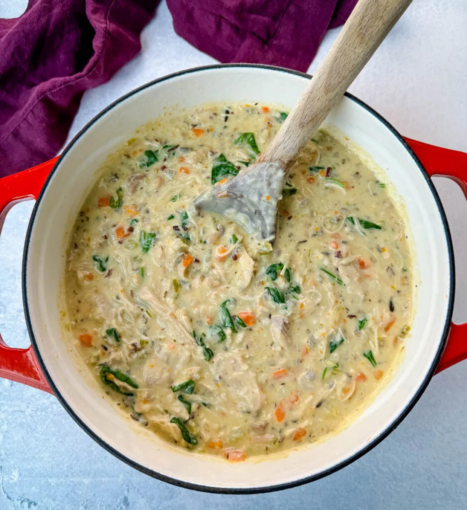 creamy chicken wild rice soup in a red Dutch oven with a wooden spoon