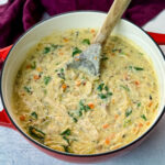 creamy chicken wild rice soup in a red Dutch oven with a wooden spoon