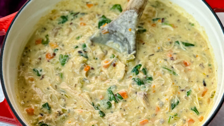 creamy chicken wild rice soup in a red Dutch oven with a wooden spoon