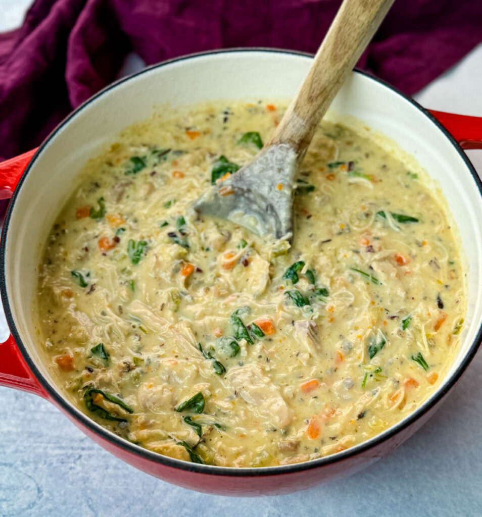 creamy chicken wild rice soup in a red Dutch oven with a wooden spoon