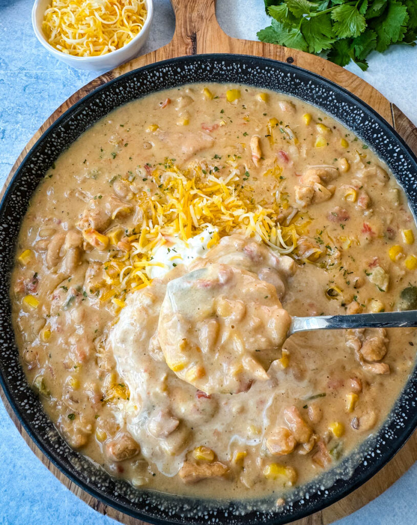 white chicken chili in a black bowl with a spoon and sour cream and grated cheese