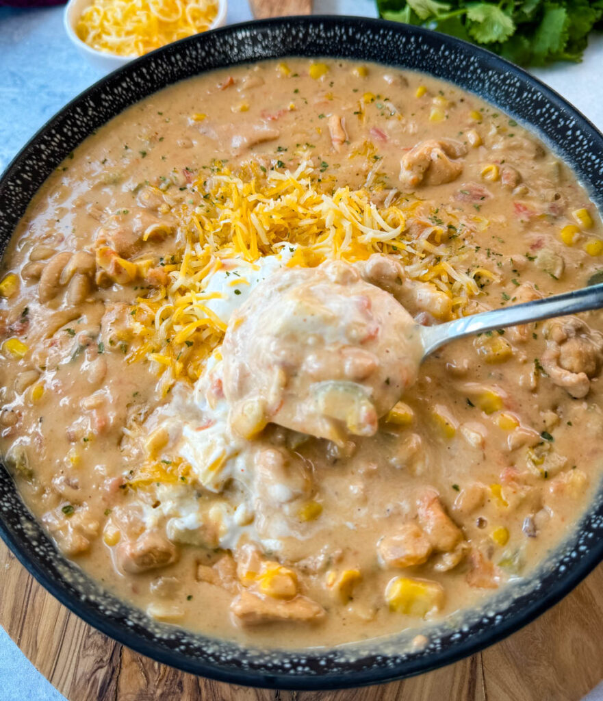 white chicken chili in a black bowl with a spoon and sour cream and grated cheese