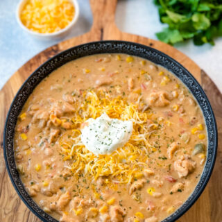 white chicken chili in a black bowl with sour cream and grated cheese