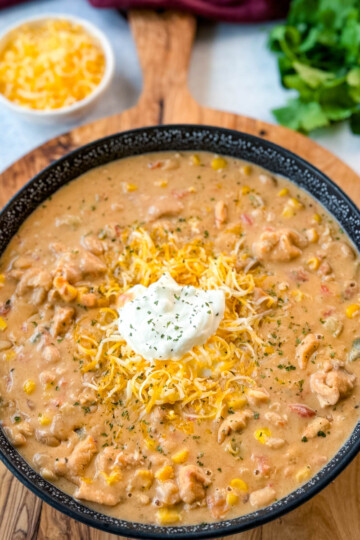 white chicken chili in a black bowl with sour cream and grated cheese