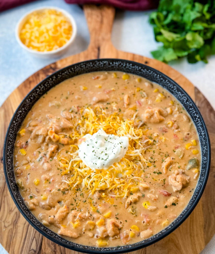 white chicken chili in a black bowl with sour cream and grated cheese