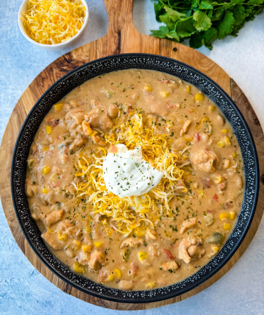 white chicken chili in a black bowl with sour cream and grated cheese