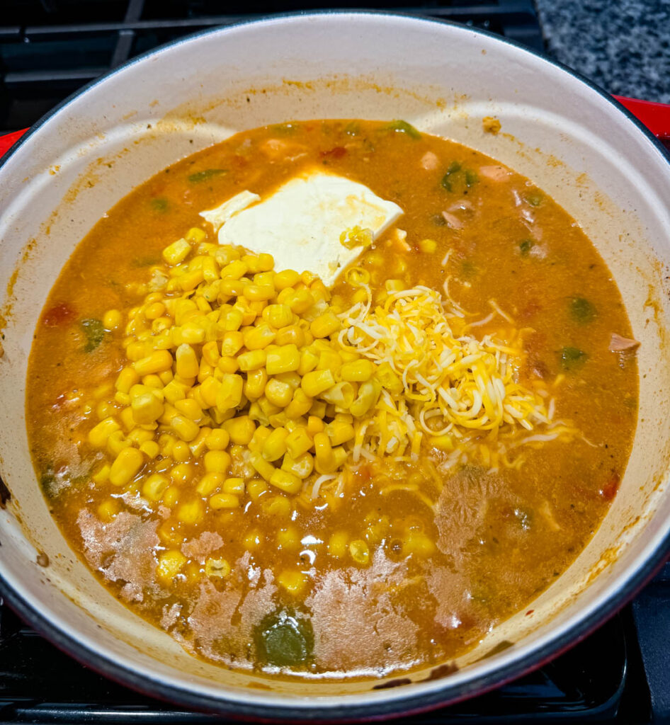 white chicken chili in a Dutch oven with cream cheese, grated cheese, and corn