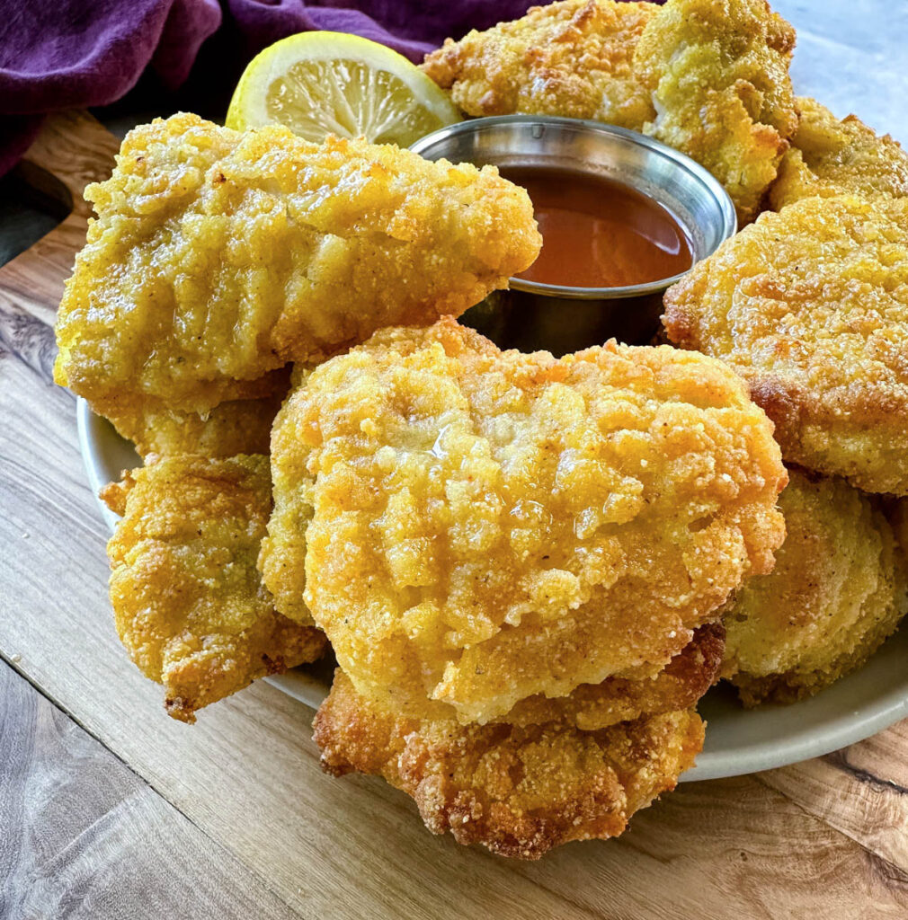 breaded catfish nuggets on a plate with hot sauce and a fresh lemon