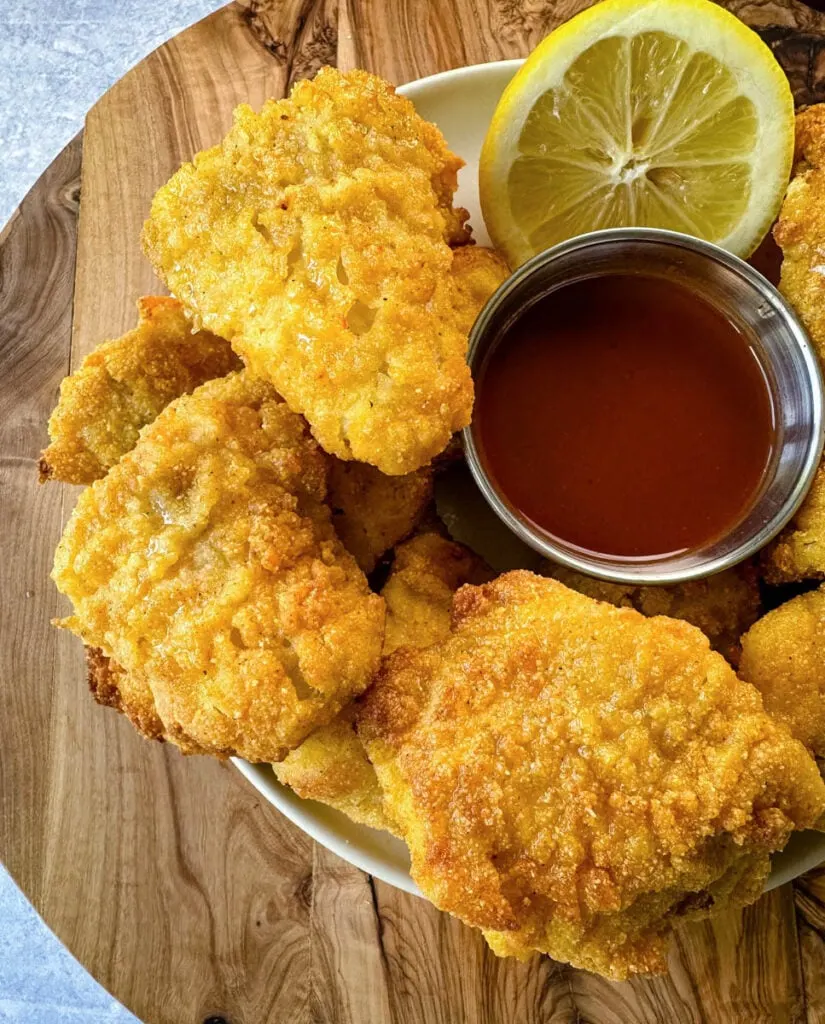 breaded catfish nuggets on a plate with hot sauce and a fresh lemon