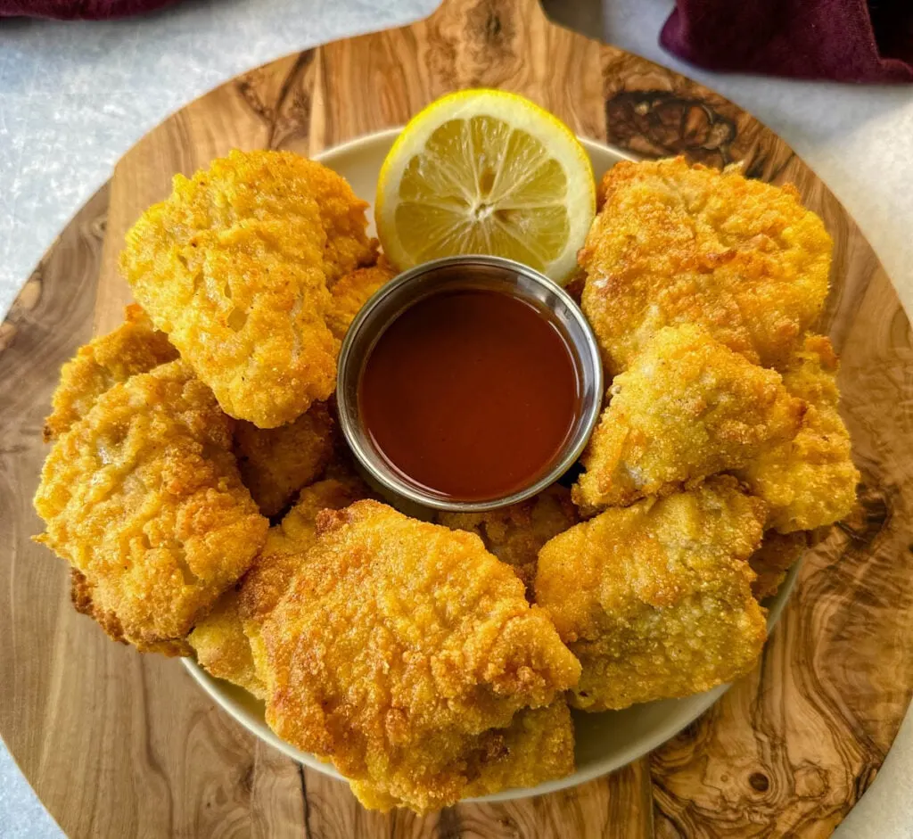 breaded catfish nuggets on a plate with hot sauce and a fresh lemon