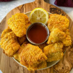 breaded catfish nuggets on a plate with hot sauce and a fresh lemon