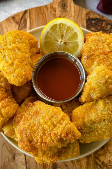 breaded catfish nuggets on a plate with hot sauce and a fresh lemon