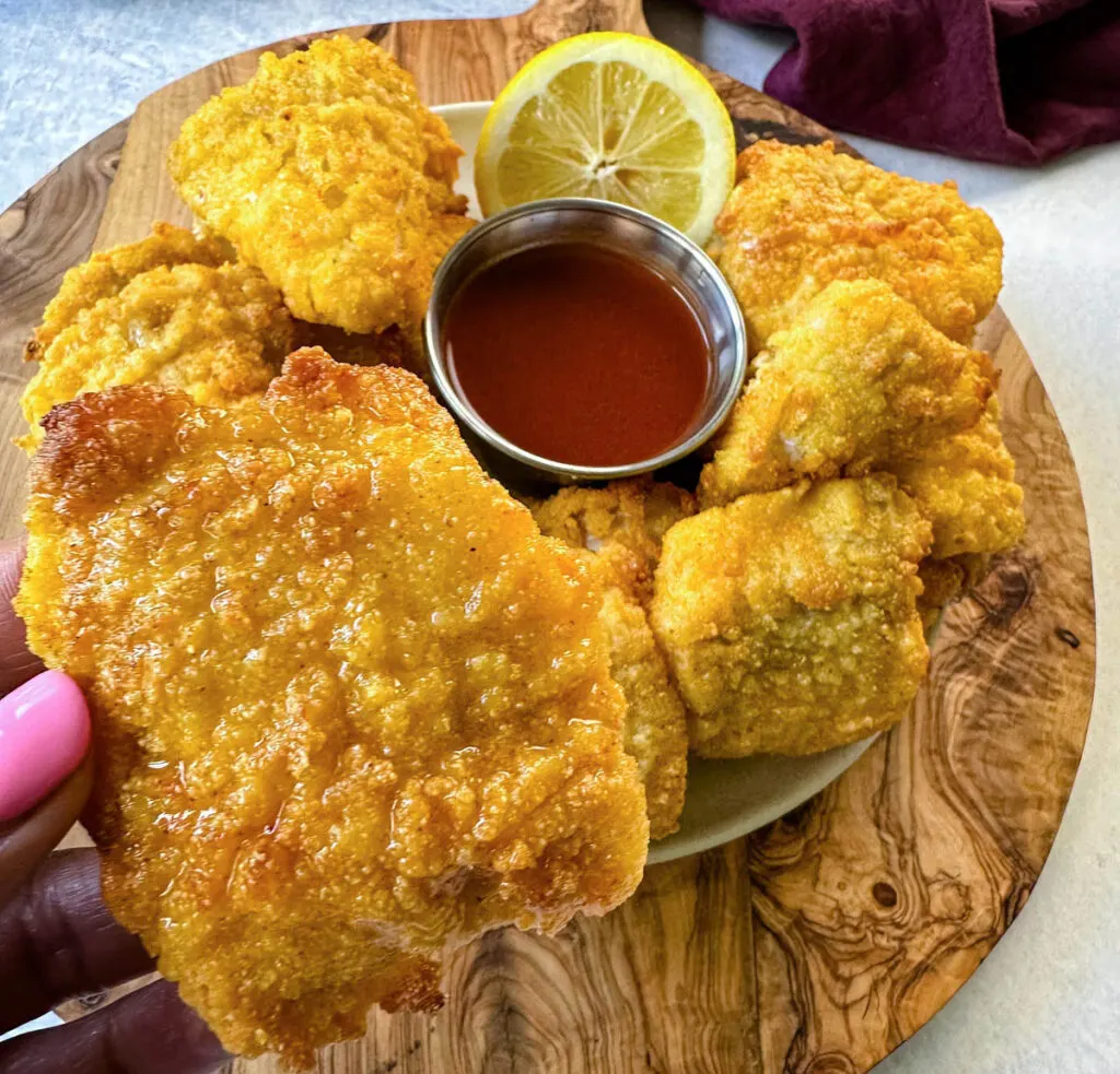 breaded catfish nuggets on a plate with hot sauce and a fresh lemon