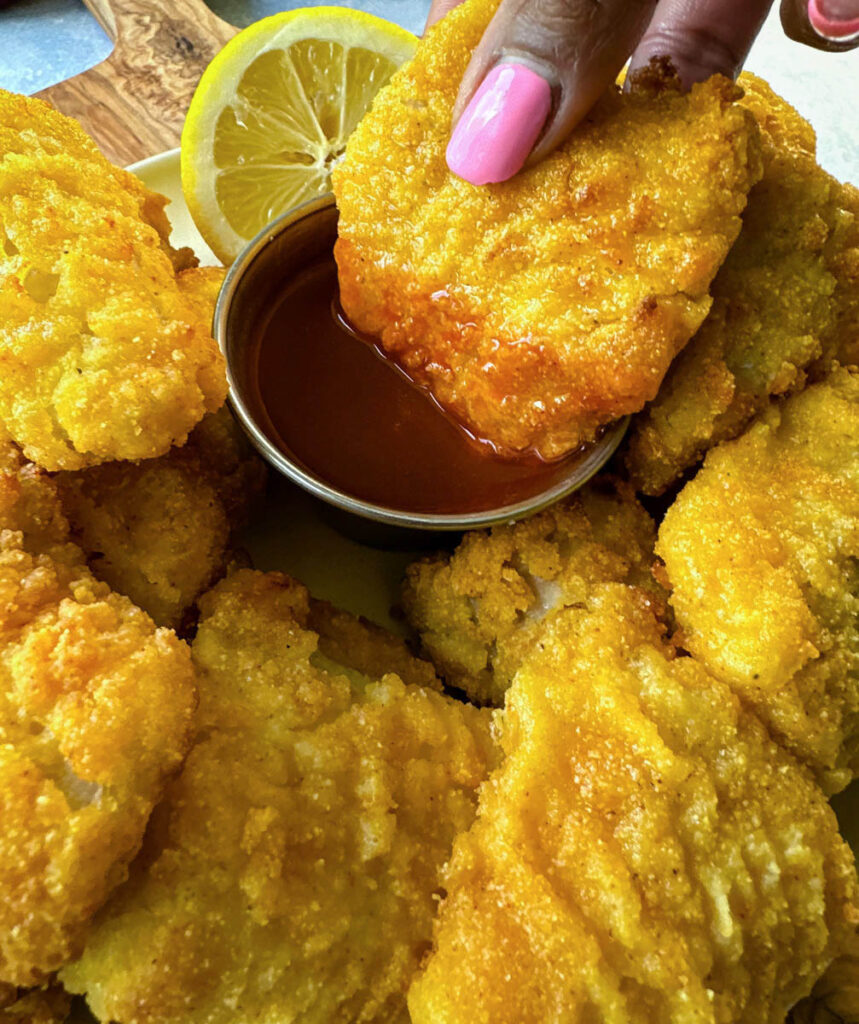 person holding catfish nugget dipped in hot sauce